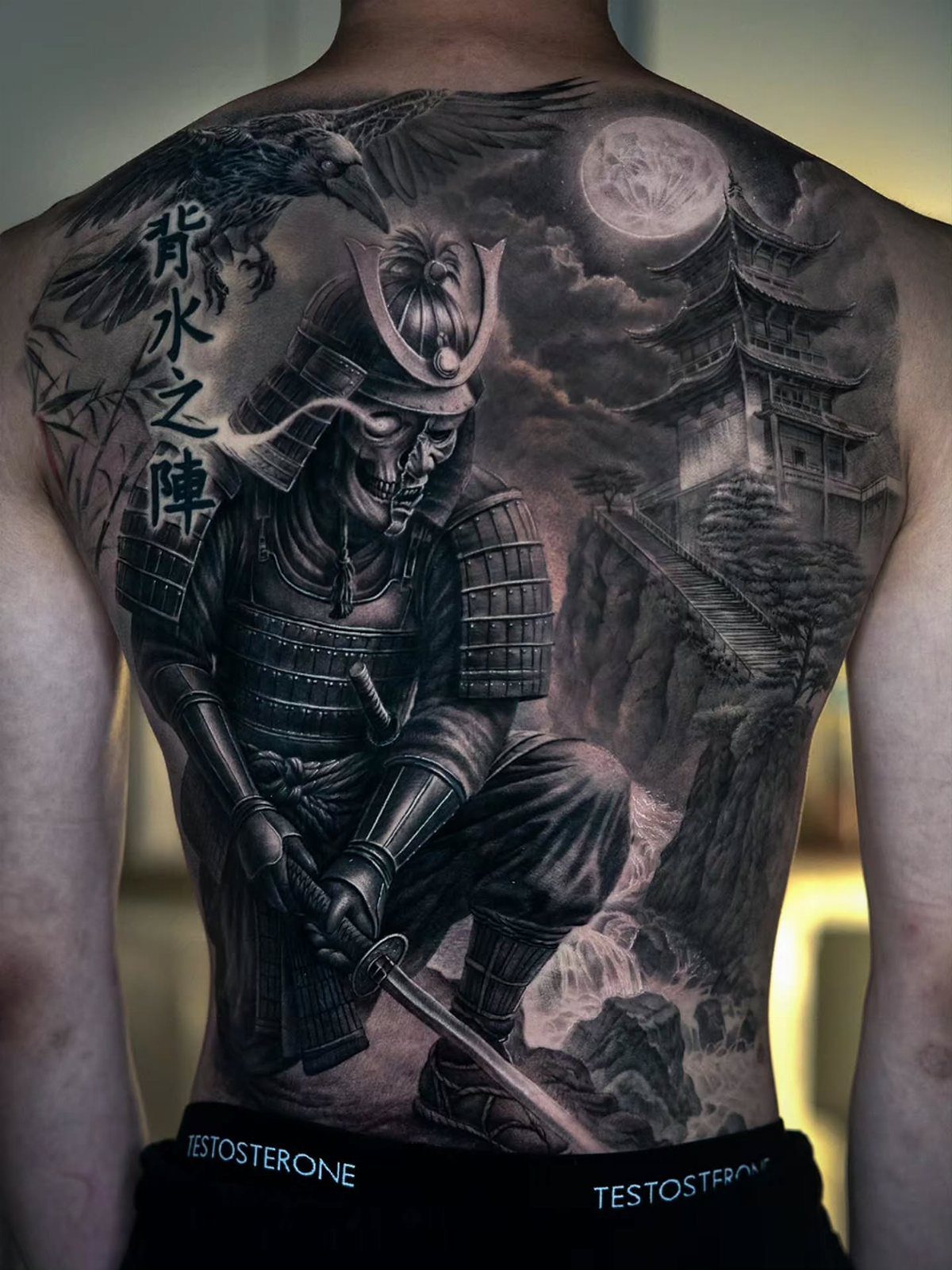 A large black and grey samurai backpiece tattoo featuring a warrior in armor with a crow and pagoda.