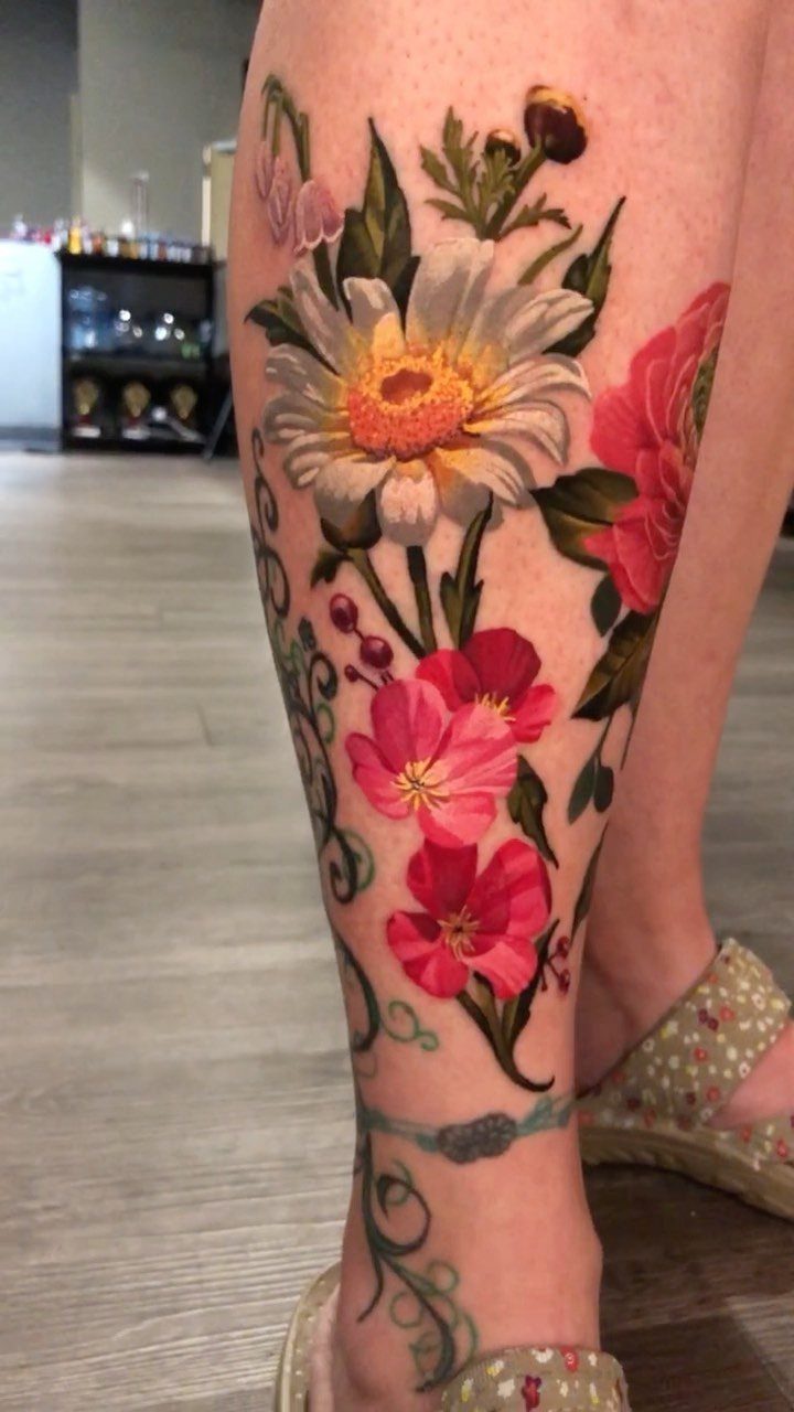 13 Large Flower Tattoo Ideas for Your Next Big Bloom 6 A large colorful floral tattoo on a leg featuring a white daisy and pink flowers.