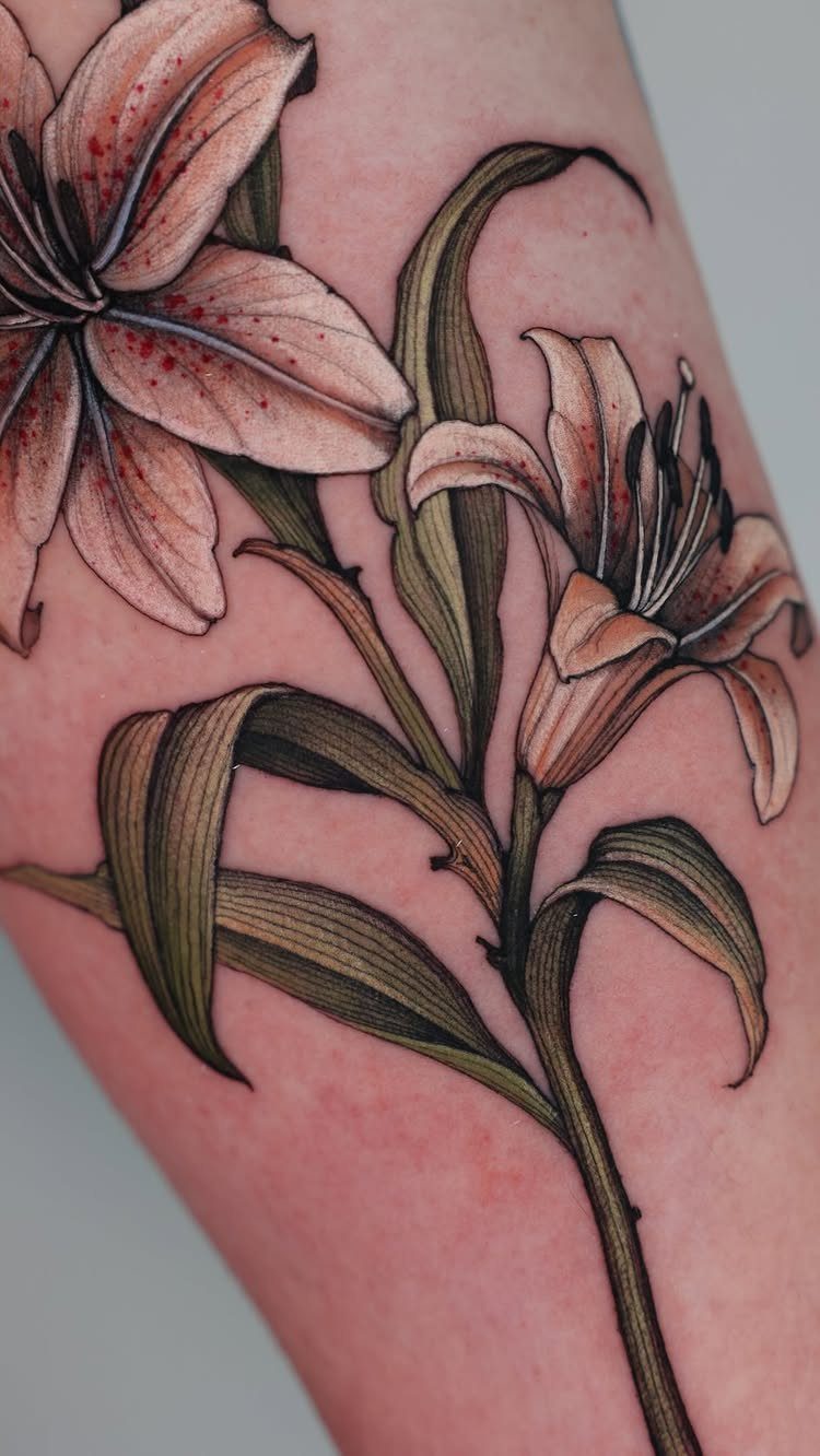 13 Large Flower Tattoo Ideas for Your Next Big Bloom 7 A large detailed tattoo of two pink lilies with green leaves on skin.