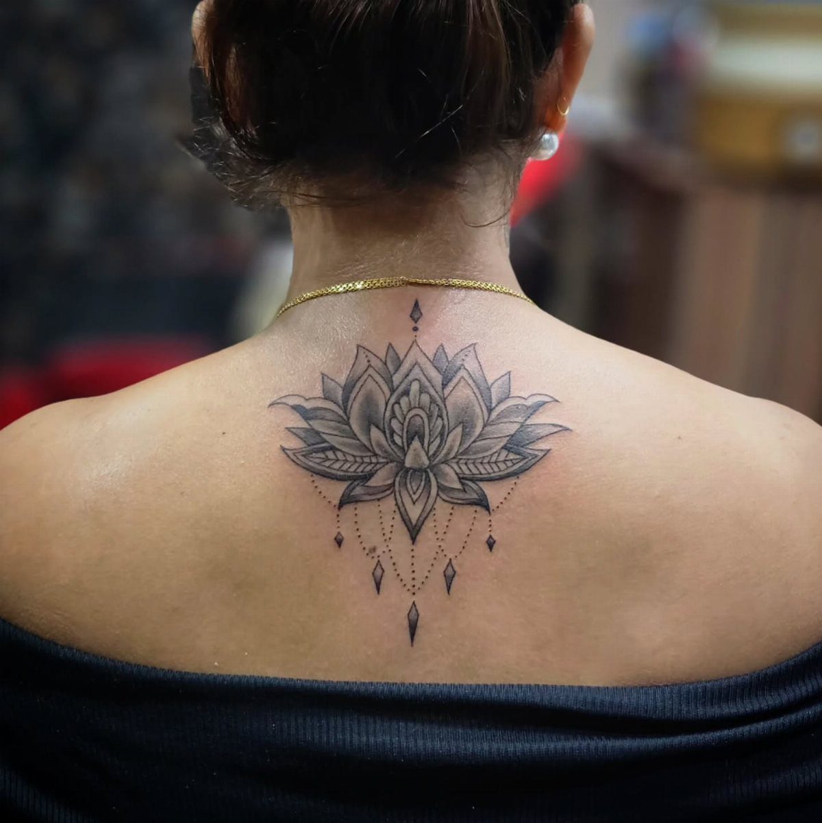 13 Large Flower Tattoo Ideas for Your Next Big Bloom 3 A black and grey lotus flower tattoo with geometric bead details on a person's upper back.