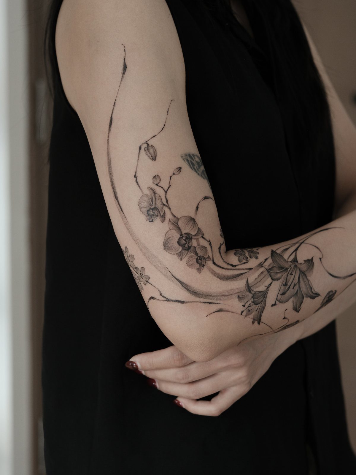13 Large Flower Tattoo Ideas for Your Next Big Bloom 12 A large black and grey orchid tattoo flowing along a person's arm and forearm.