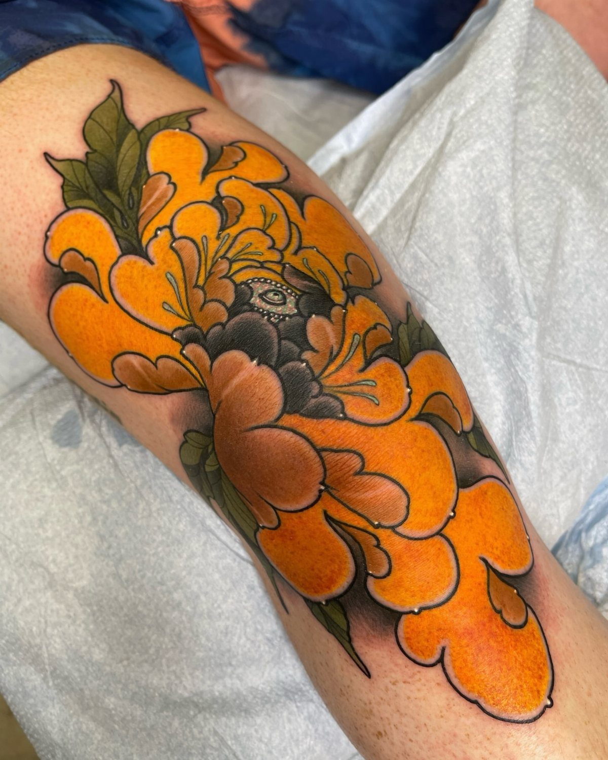 13 Large Flower Tattoo Ideas for Your Next Big Bloom 5 Large orange peony tattoo with green leaves on a person's leg.
