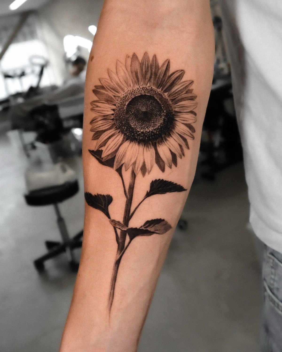13 Large Flower Tattoo Ideas for Your Next Big Bloom 4 A detailed black and grey sunflower tattoo on a person's forearm.