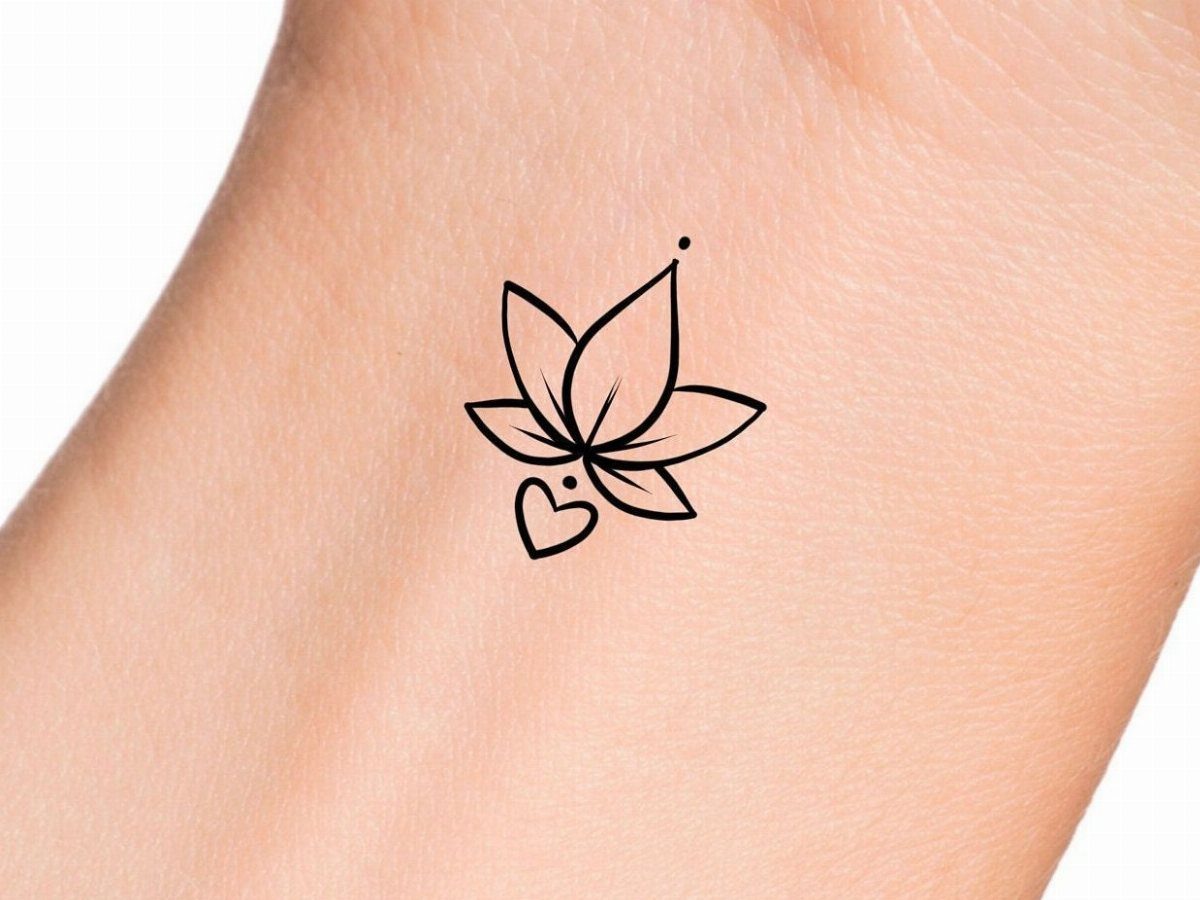 A minimalist black ink lotus flower tattoo with a small heart shape on skin.