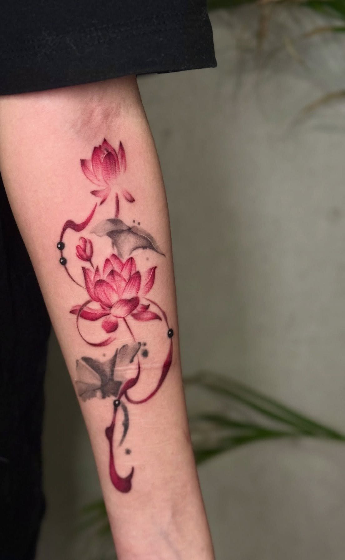 Red lotus flower tattoo with swirling vines and leaves on a person's forearm.