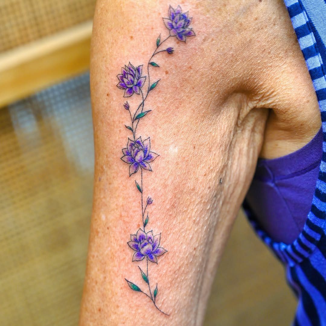 A vertical purple lotus flower and vine tattoo on a person's arm.