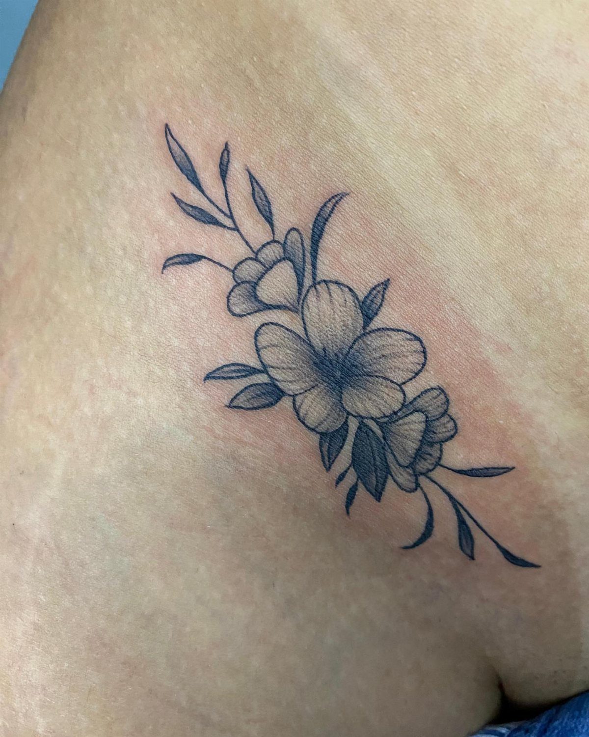 Fine line black ink tattoo of flowers and leaves on human skin.