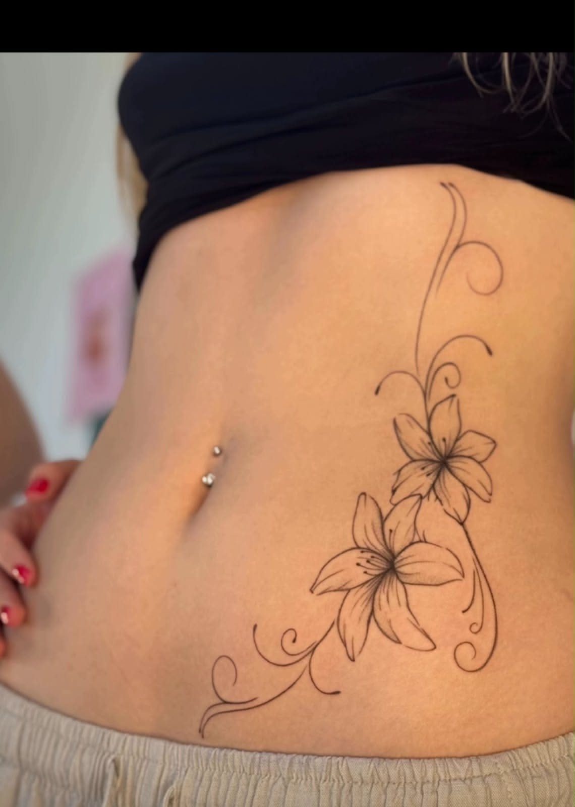 A floral tattoo with two lilies and swirling vines on a woman's stomach.