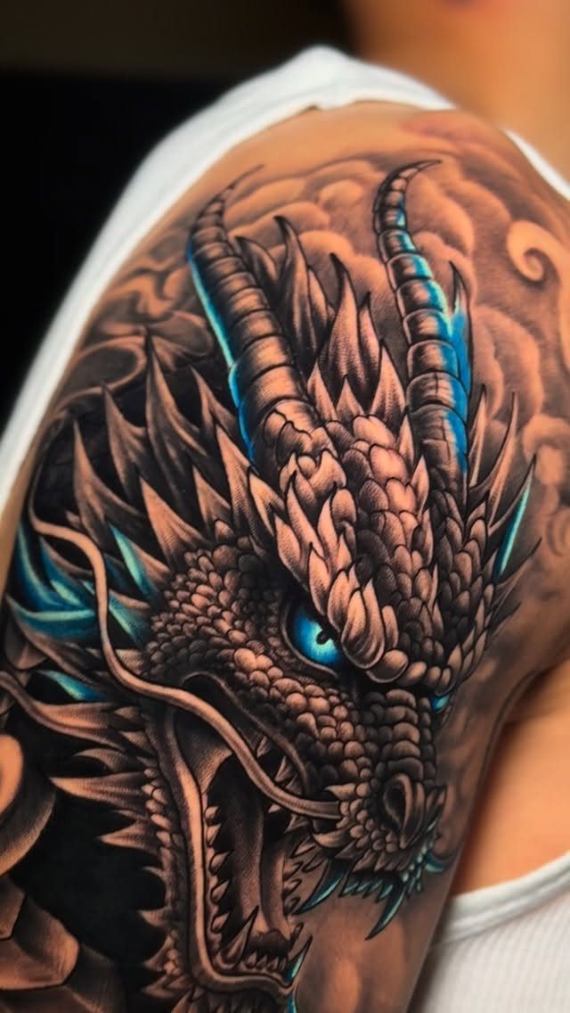 A detailed dragon head tattoo with blue accents on a person's shoulder.