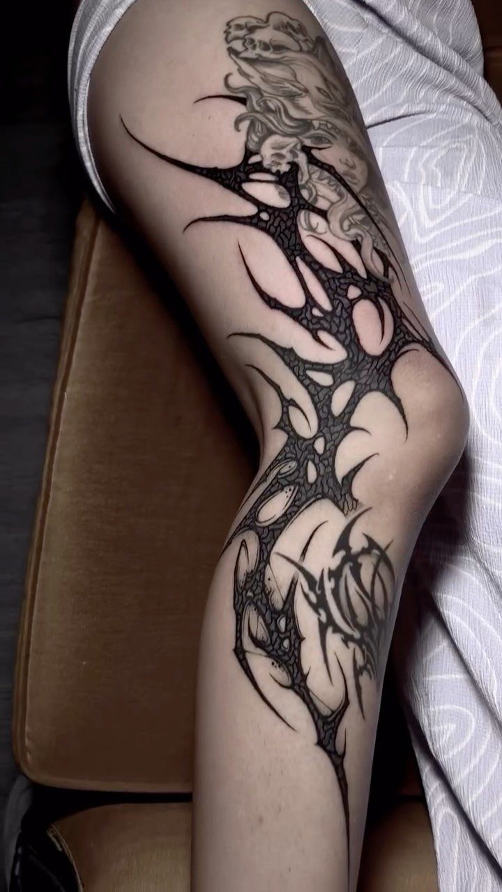 Black neo-tribal tattoos with sharp, flowing lines wrap around a person's leg and knee.