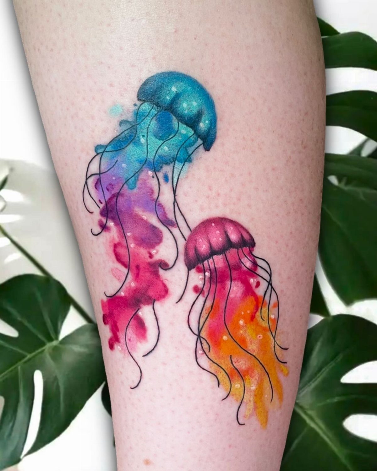 10 Ocean Themed Tattoos: From Fine Line Turtles to Black and Grey Mantas 4 Two colorful watercolor jellyfish tattoos with flowing tentacles on a person's leg.