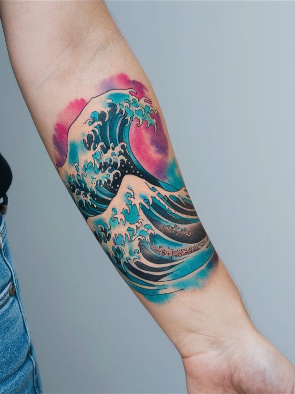 10 Ocean Themed Tattoos: From Fine Line Turtles to Black and Grey Mantas 10 A large forearm tattoo of blue ocean waves with a pink watercolor background.