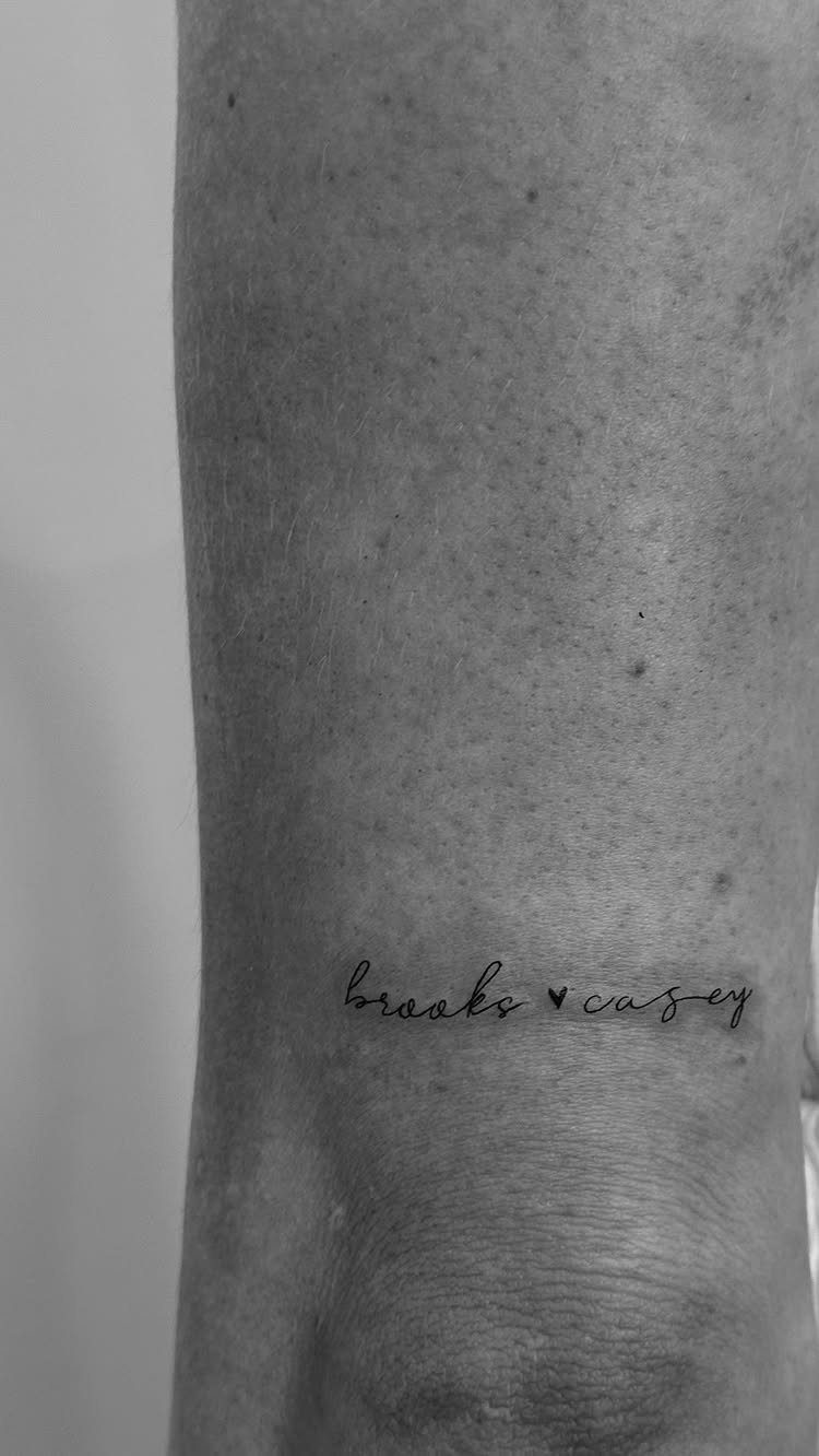 A small cursive script tattoo of two names with a heart on skin.