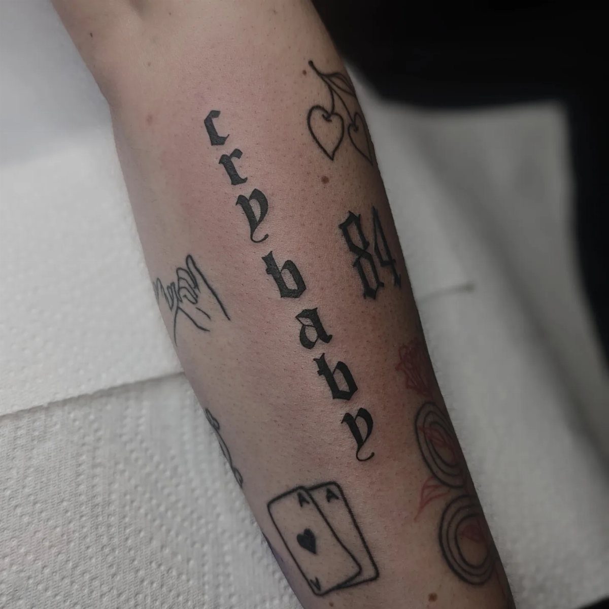Arm with various black ink tattoos including the word crybaby in gothic lettering.