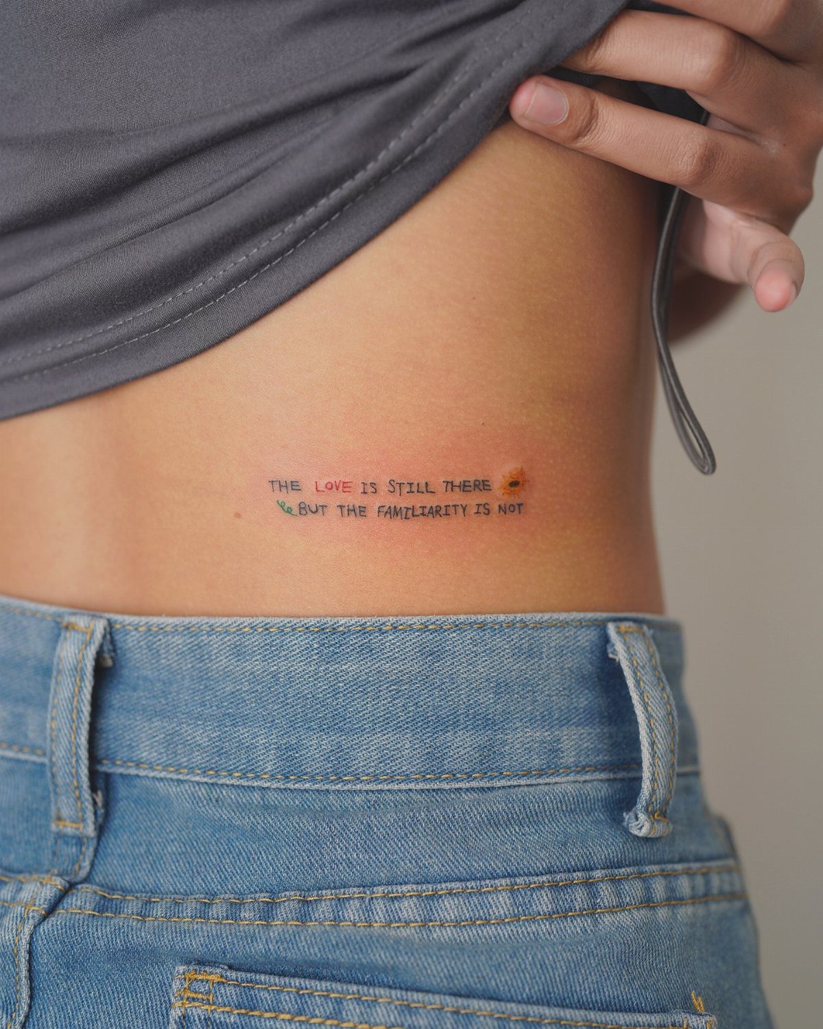 A small minimalist sans-serif text tattoo on a person's skin above blue denim jeans.