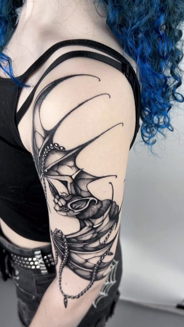 A large black ink bat tattoo with decorative chains on a person's upper arm.