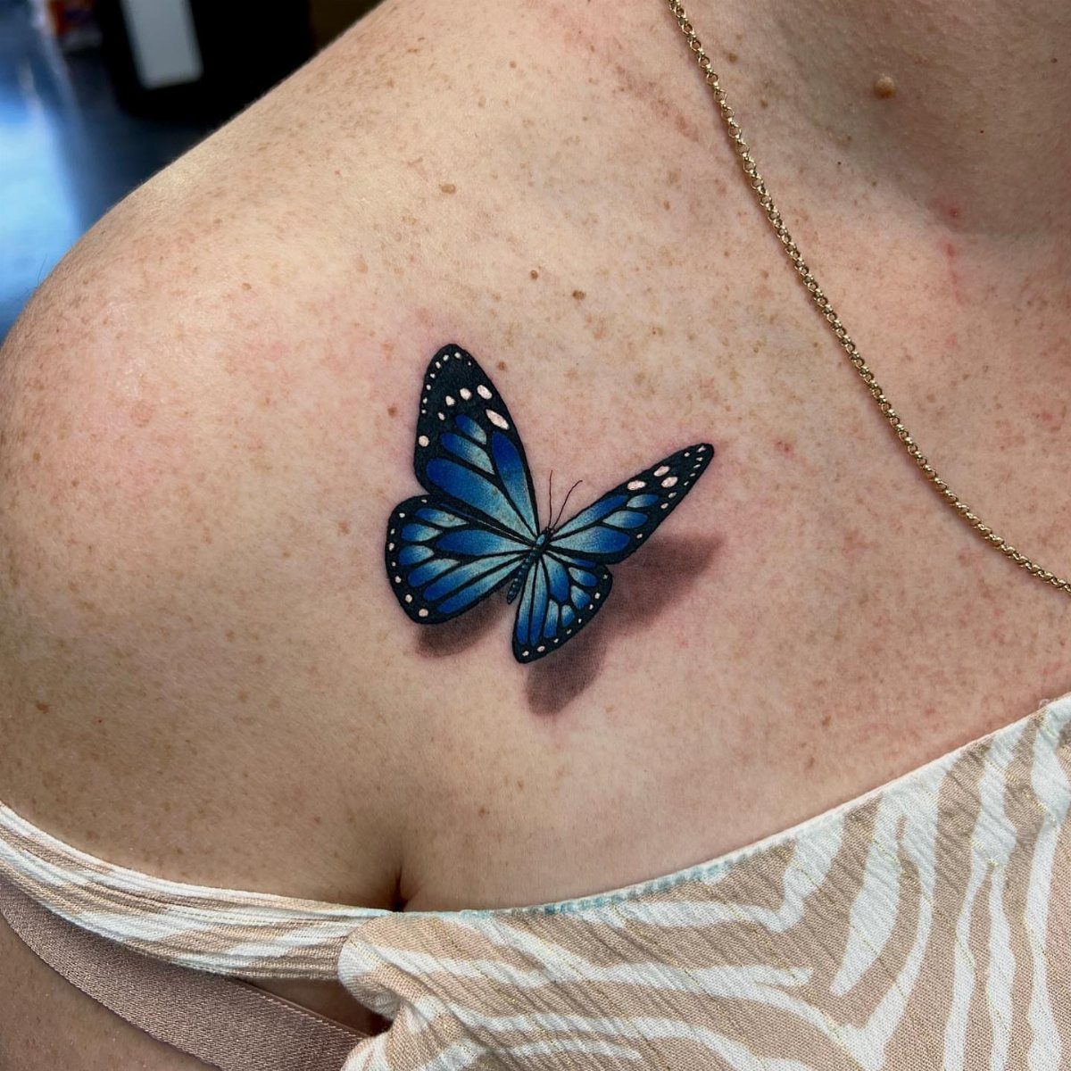 A blue and black butterfly tattoo on a person's skin near the collarbone.