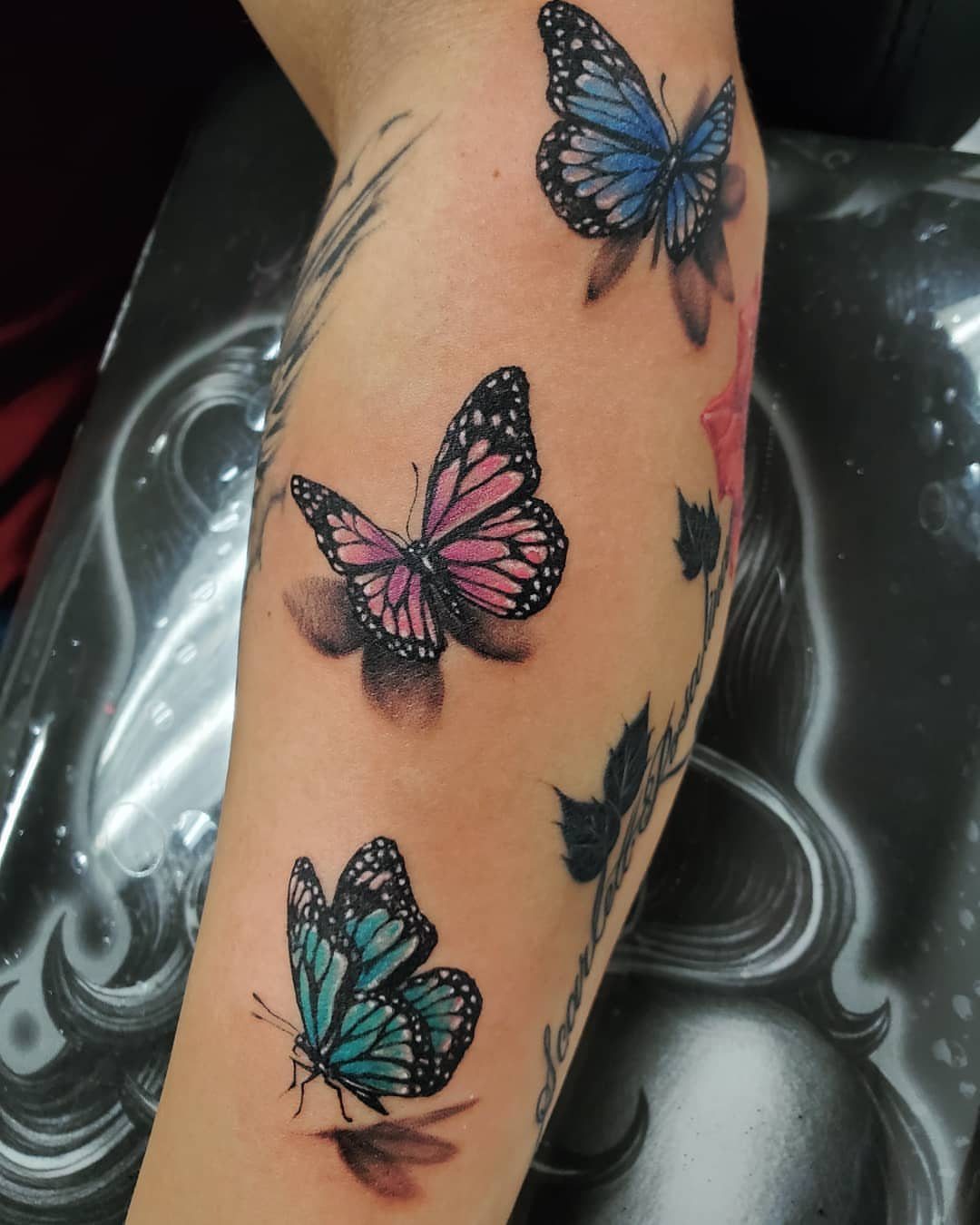 Three colorful butterfly tattoos in blue, pink, and teal on a person's forearm.