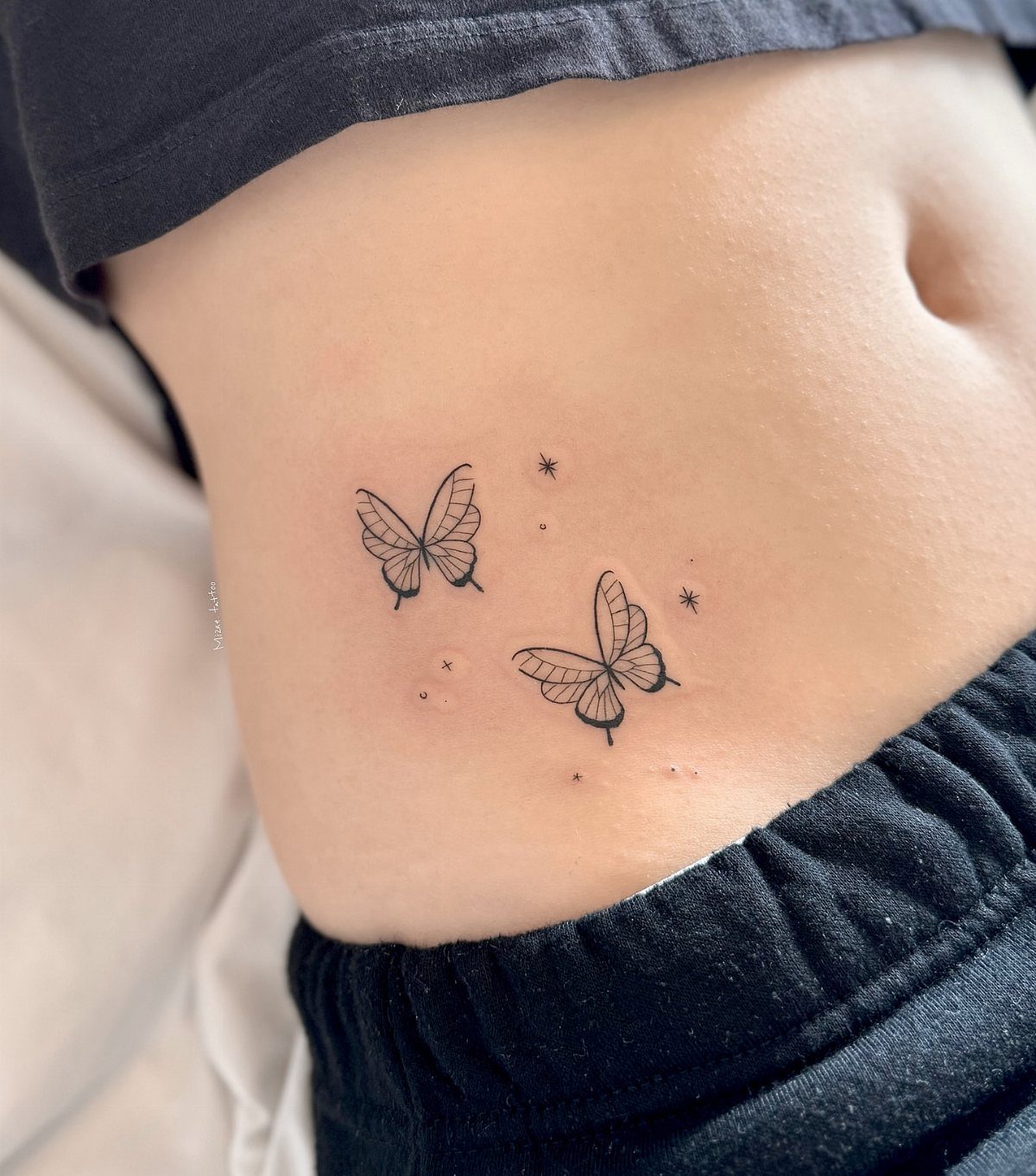 Two small minimalist butterfly tattoos with fine lines and stars on a person's skin.