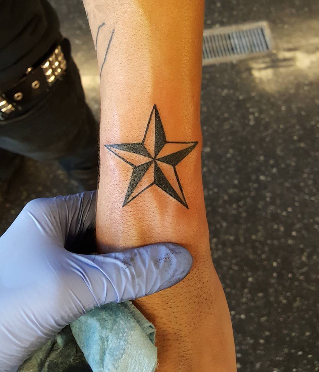 A black ink nautical star tattoo with shaded facets on a person's wrist.