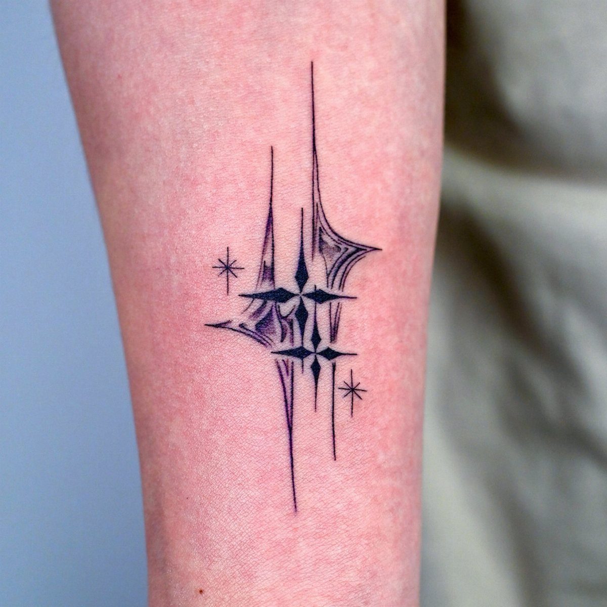 An intricate black ink star tattoo with sharp geometric lines on a person's arm.