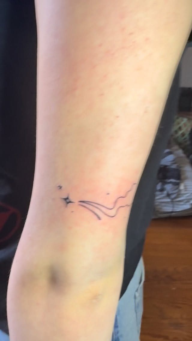 A small minimalist shooting star tattoo on a person's arm with thin wavy lines.