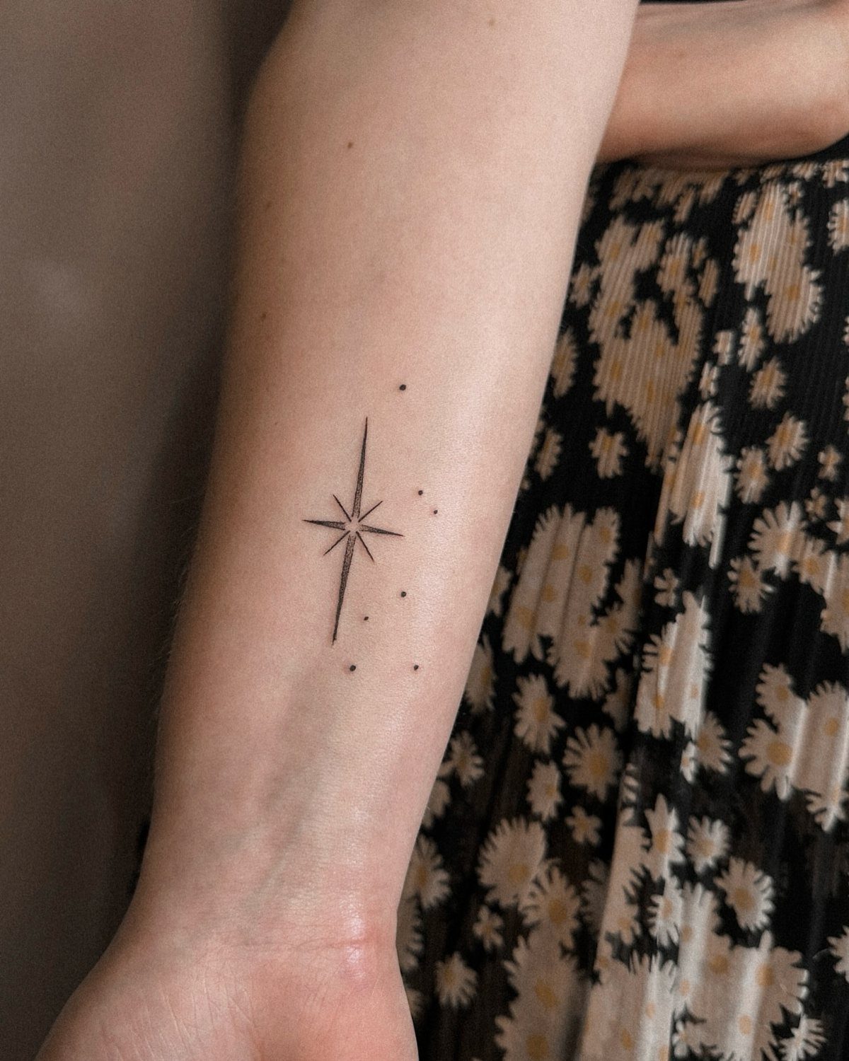 A small black fine-line star tattoo with tiny dots on a person's forearm.