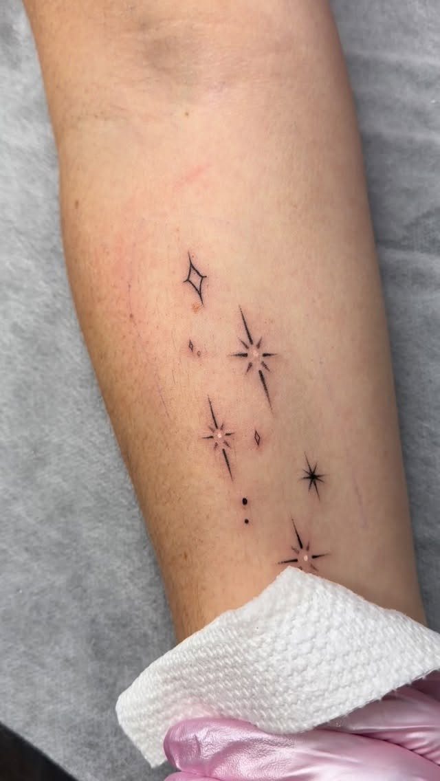 Small black ink star tattoos arranged in a cluster on a person's arm.