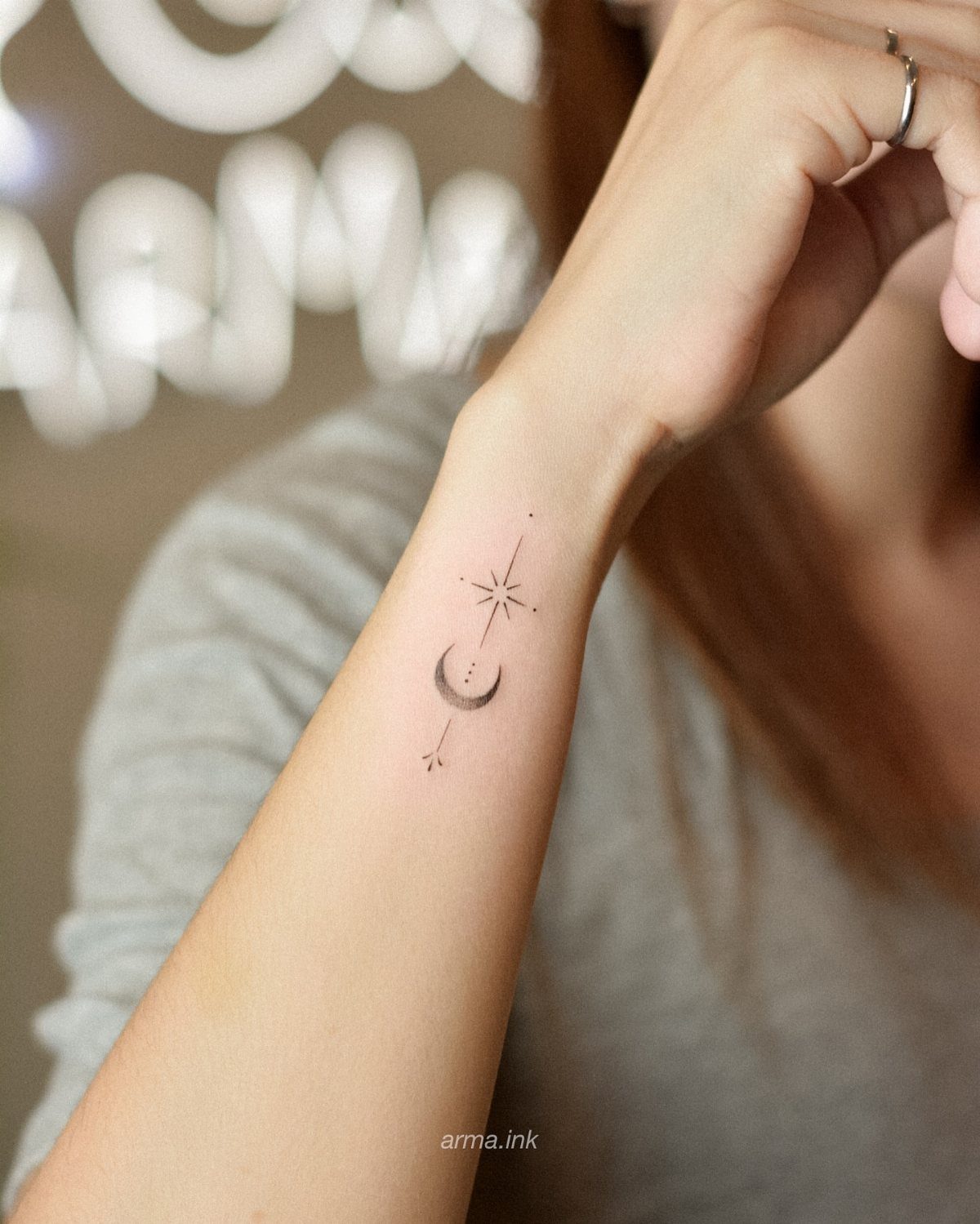 A minimalist fine line tattoo of a crescent moon and star on a person's wrist.