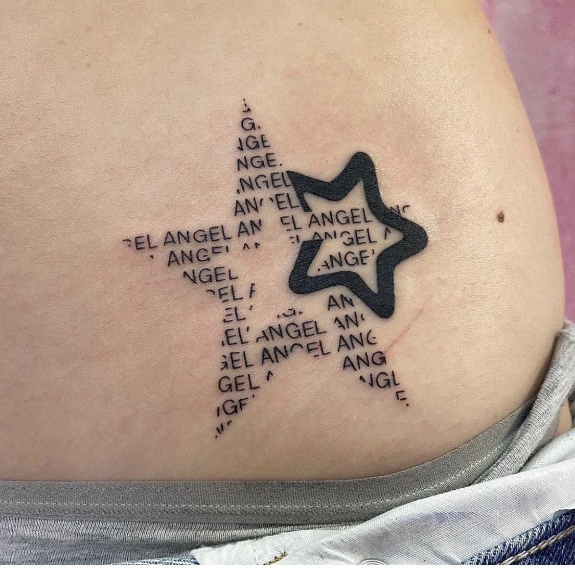 A tattoo of two stars, one outlined and one formed by the repeated word angel.