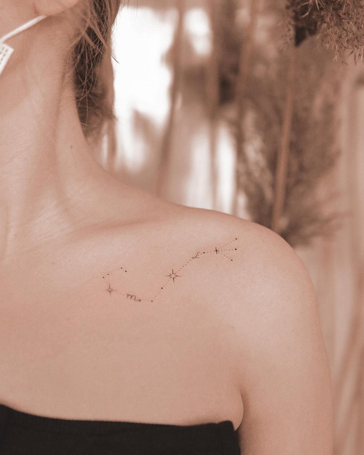 A delicate fine line constellation tattoo on a person's shoulder against a soft background.