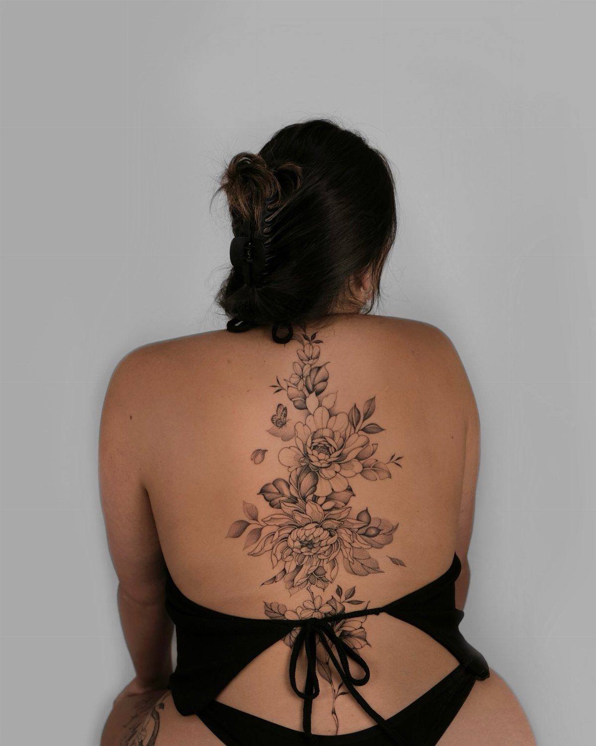 A woman's back featuring a large black ink floral vine tattoo running down her spine.