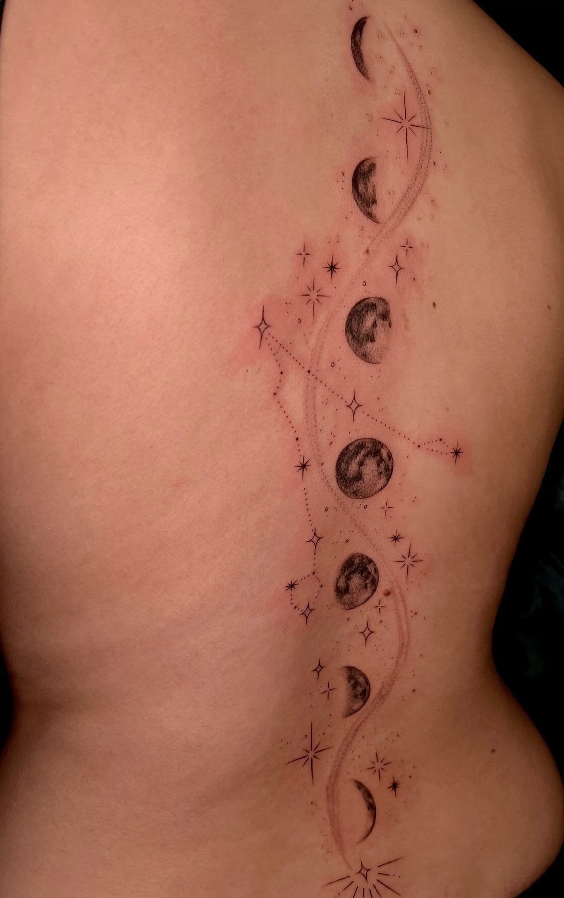 A vertical spine tattoo depicting moon phases and stars on a person's back.