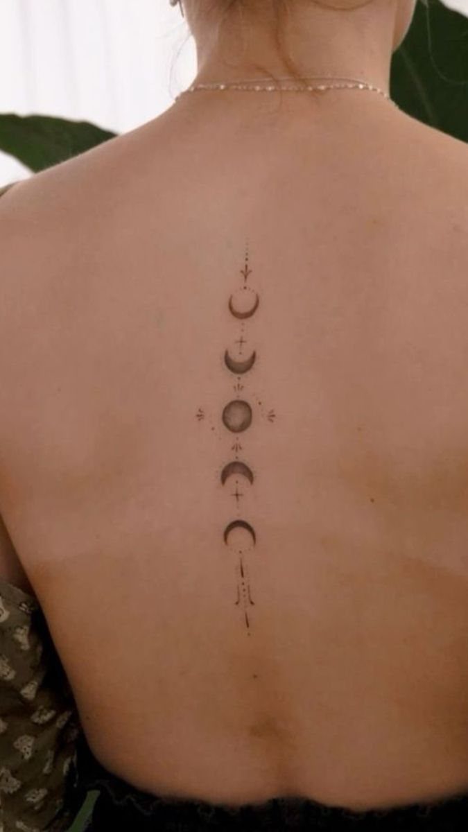 A vertical spine tattoo depicting various moon phases with delicate geometric line accents.