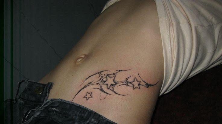 A black ink tattoo of tribal swirls and stars on a person's waist.
