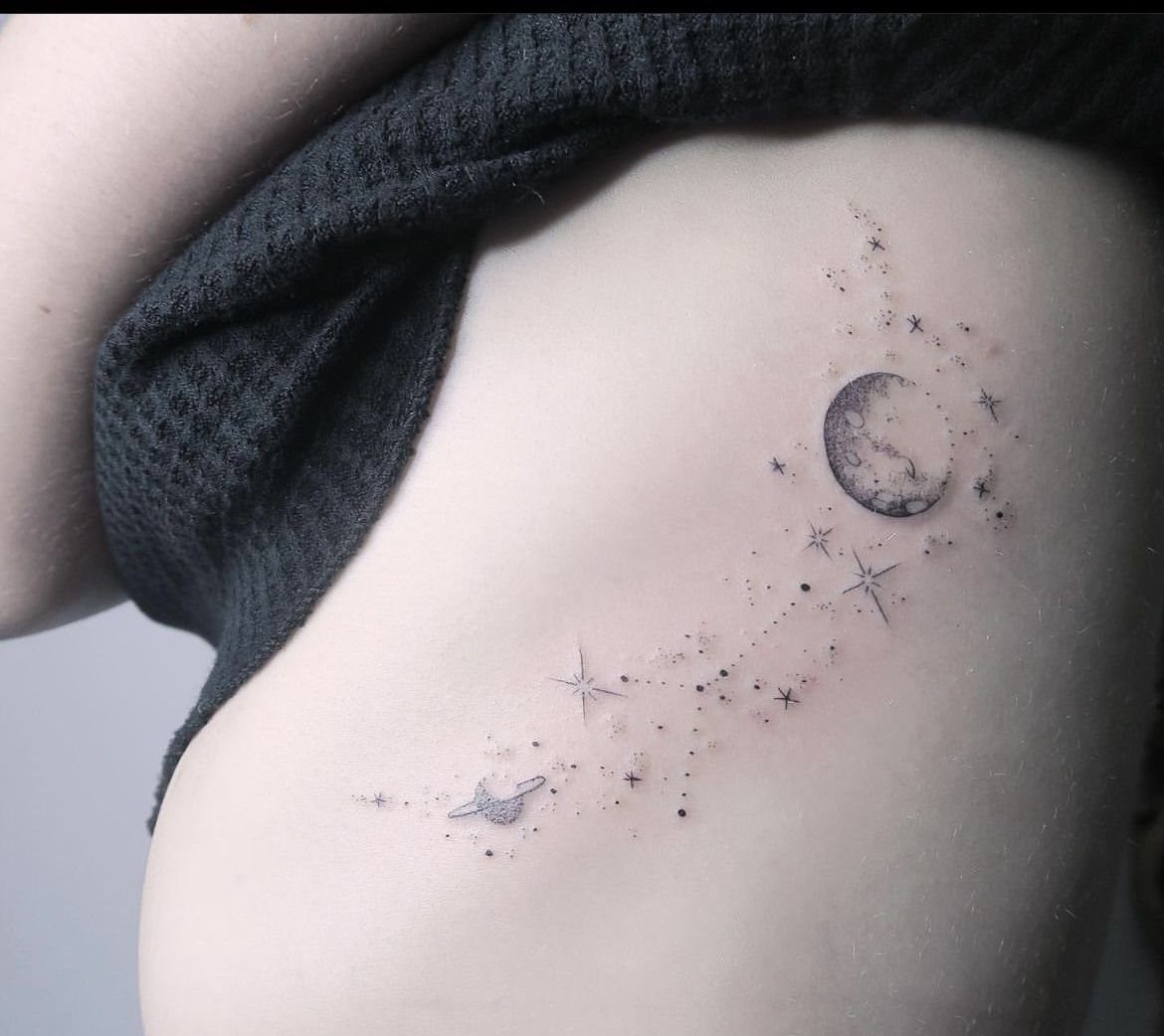 Fine-line tattoo of a crescent moon, stars, and Saturn on a person's side.