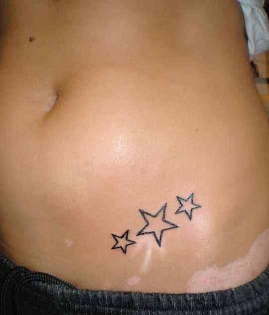 Three small black ink outline stars tattooed on a person's waist area.