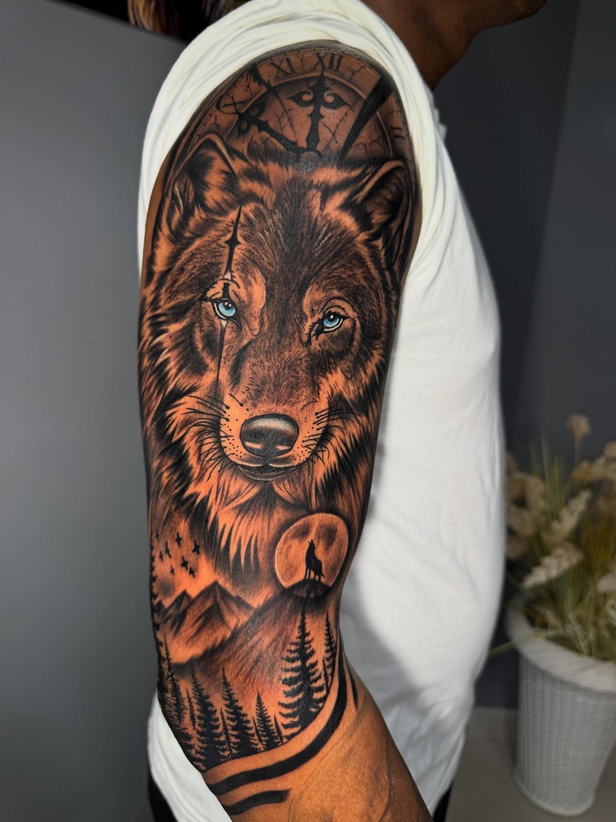 A detailed wolf head tattoo on an arm featuring mountains, a moon, and a pine forest.