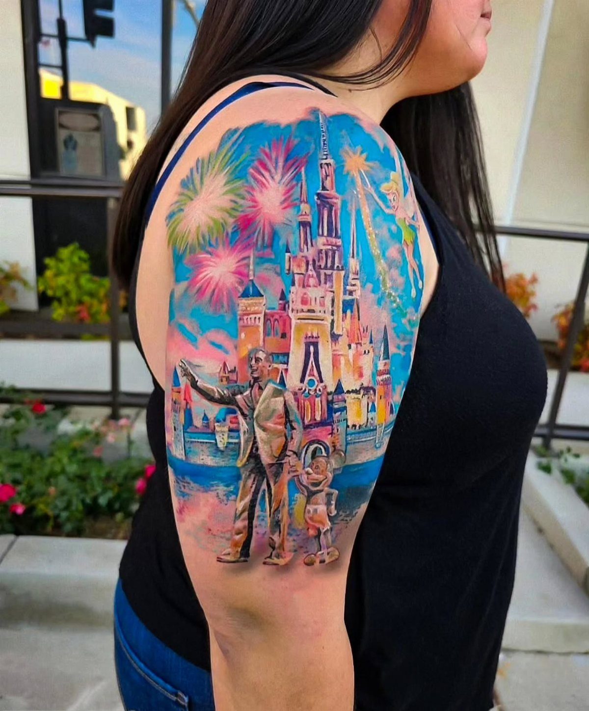 A colorful Disney themed sleeve tattoo on a person's arm featuring a castle and characters.