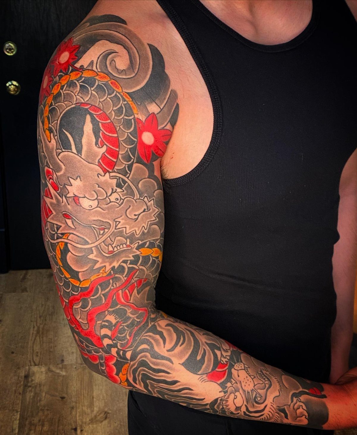 A man's arm displaying a detailed Japanese style sleeve tattoo with a dragon and red flowers.