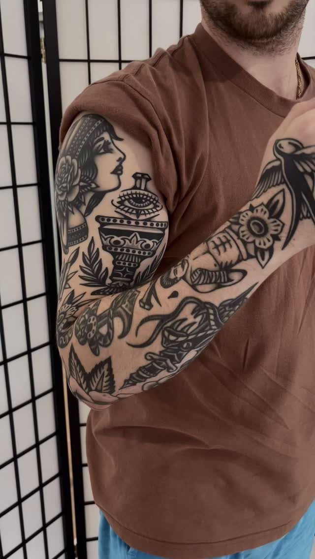 A man's arm covered in a detailed black ink traditional style sleeve tattoo.
