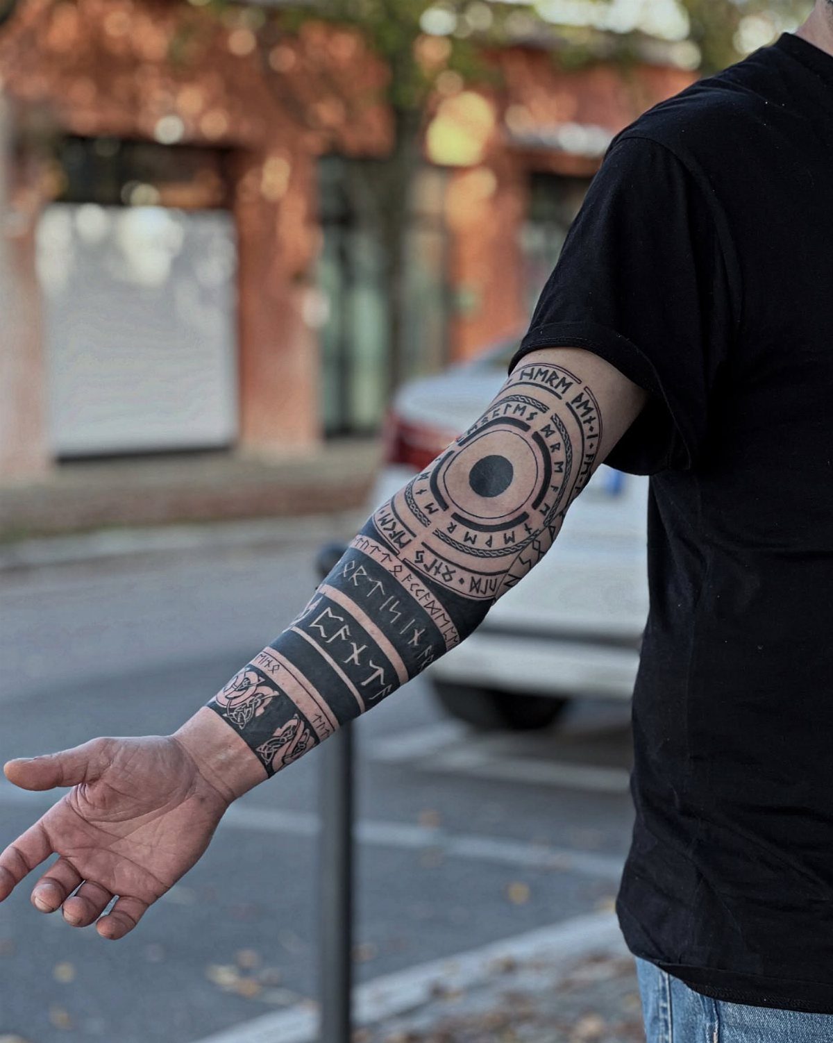 A person's forearm displaying a black ink sleeve tattoo with runic symbols and circular patterns.
