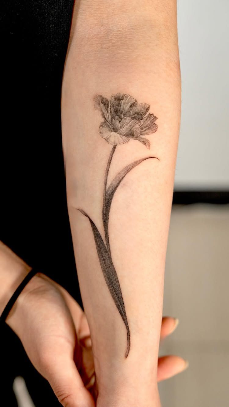 22 Tattoo Pattern Floral Ideas for Arms, Ribs & Full Sleeves 20 A black and grey tulip flower tattoo on a person's forearm with a long stem.