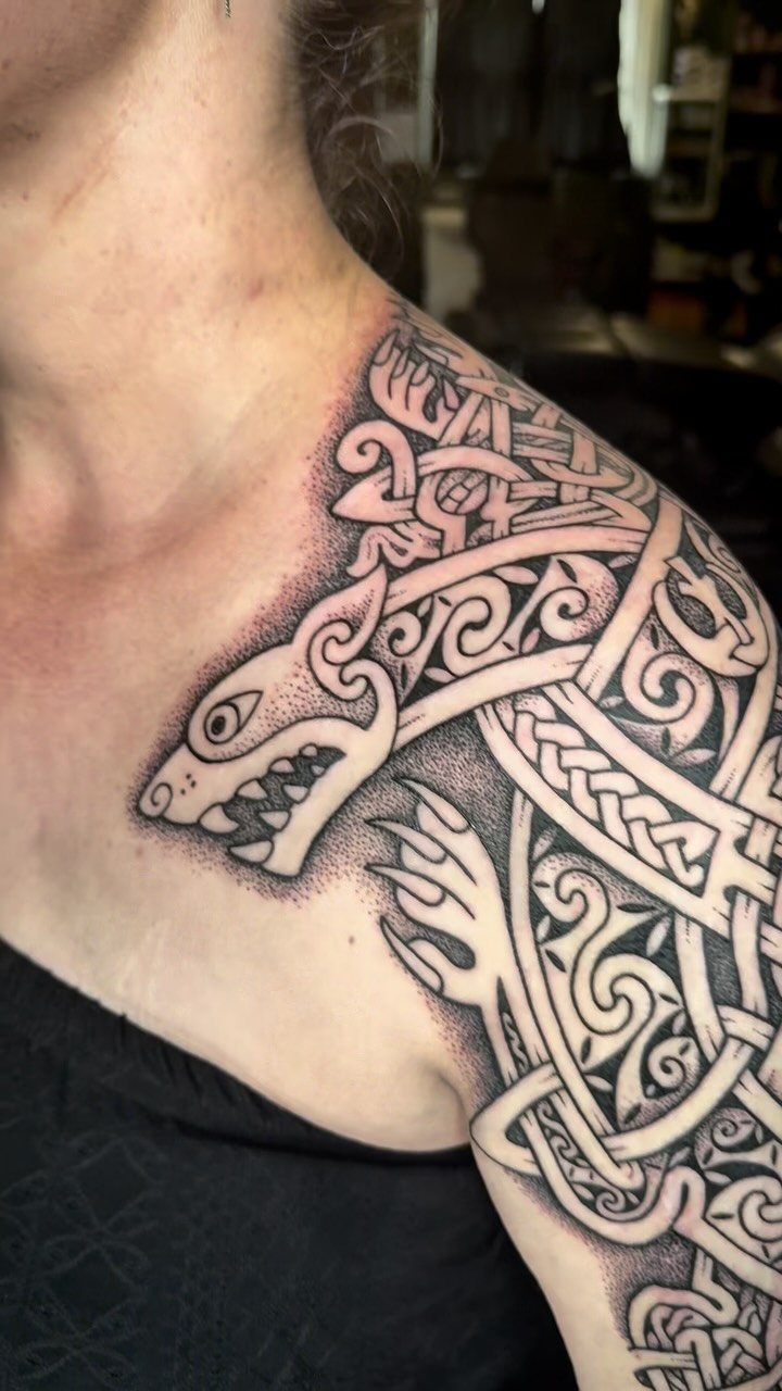 A detailed Celtic knotwork tattoo featuring a stylized animal head on a person's shoulder.