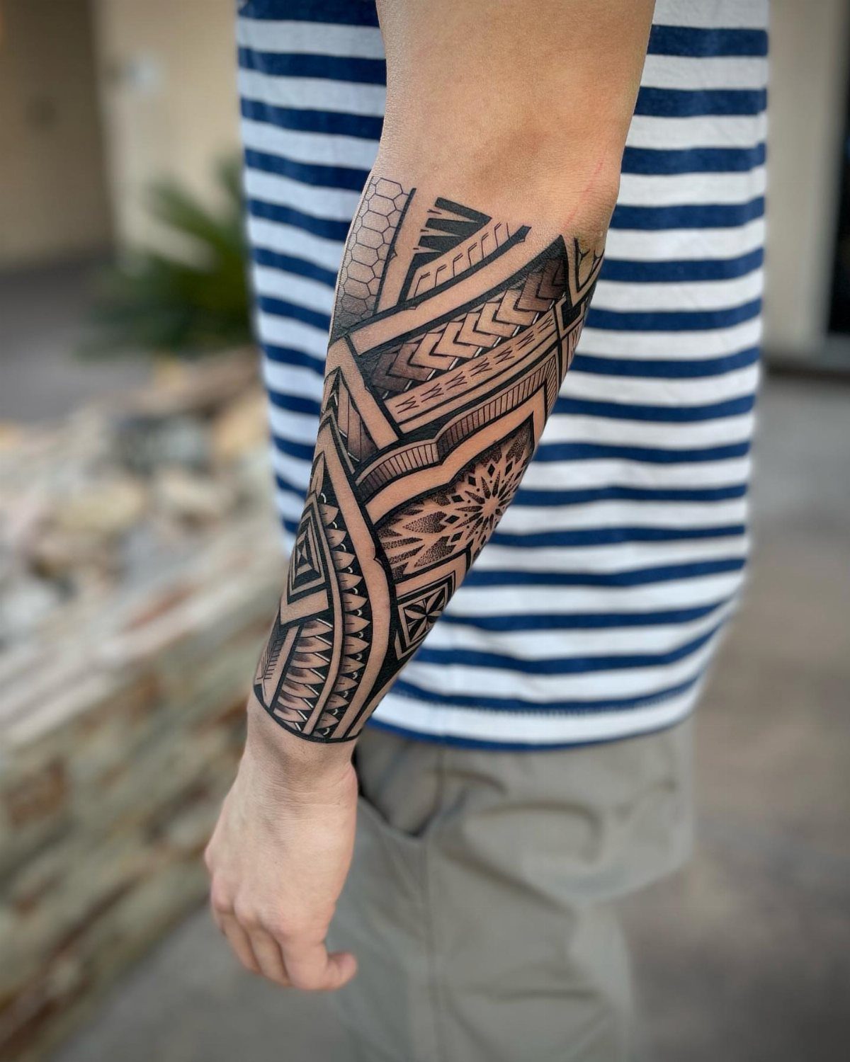 A forearm tattoo featuring complex black geometric tribal patterns on a person's skin.