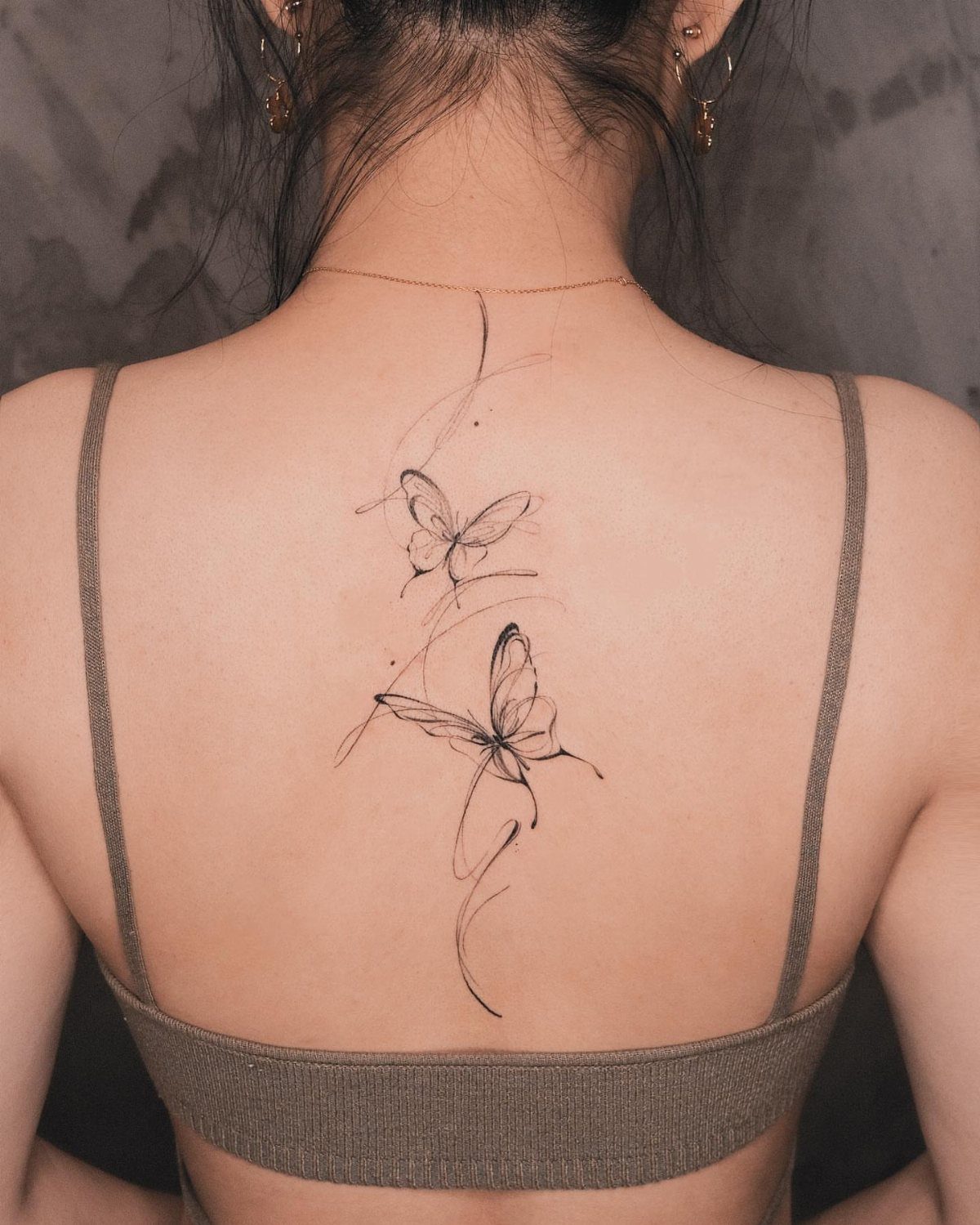 Two butterfly tattoos with flowing lines on a woman's upper back.