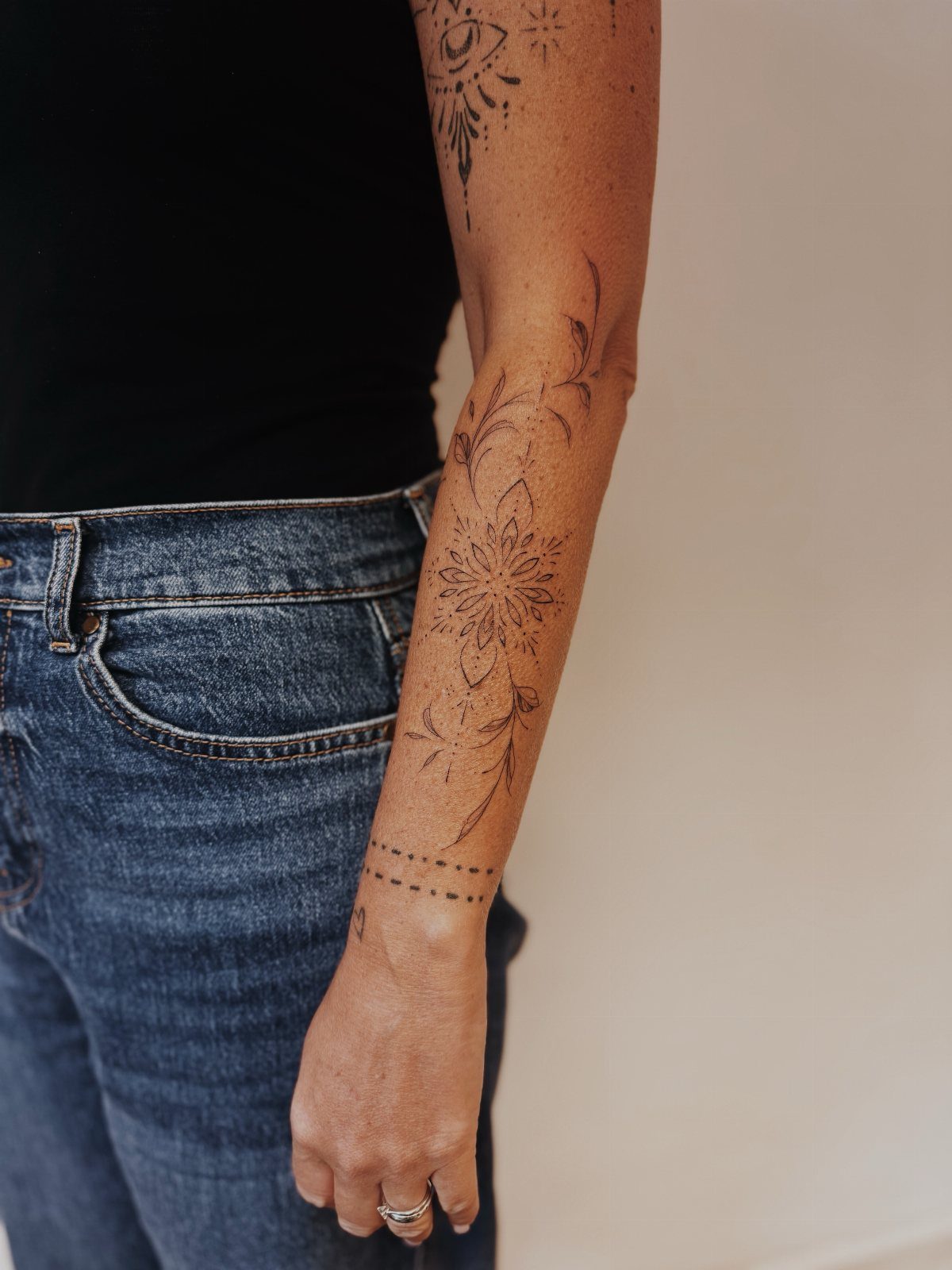 A person's arm displaying various black ink floral and geometric tattoos.