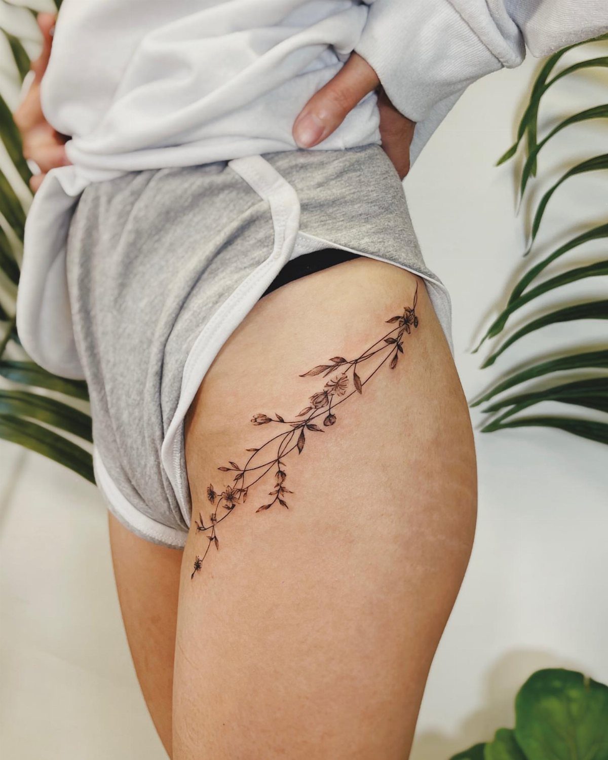 A delicate black ink floral vine tattoo stretching across a person's hip and upper thigh.