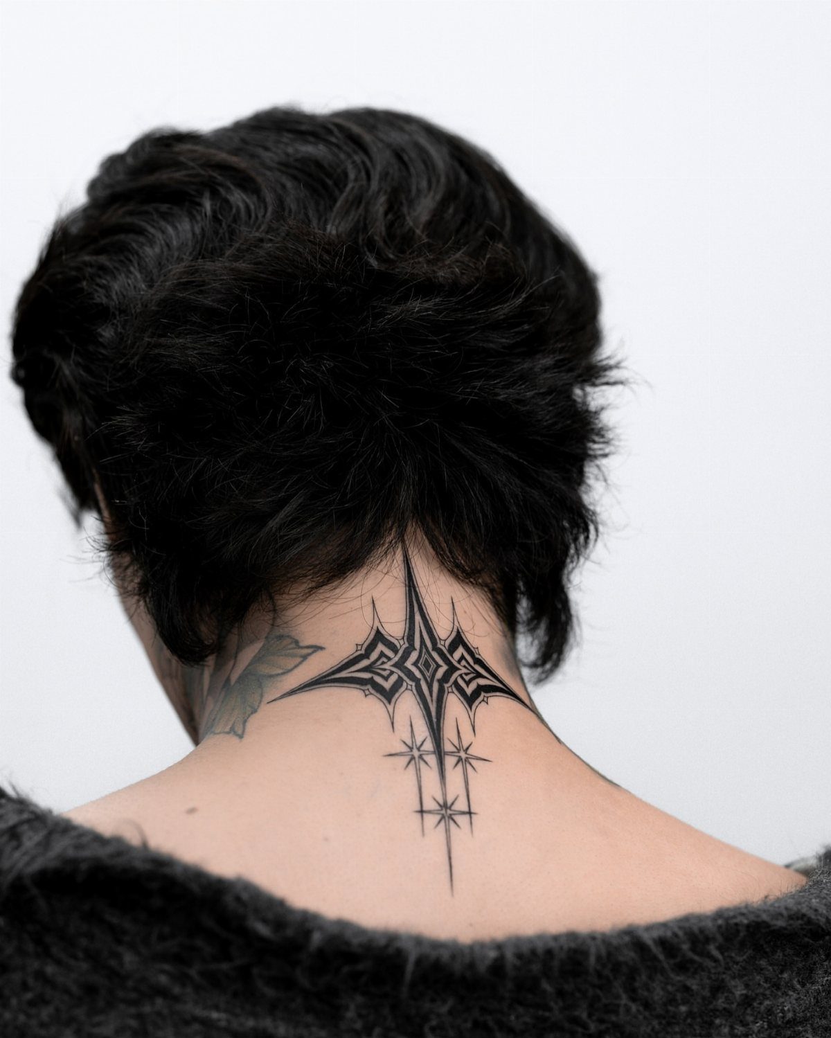 A person with short black hair displaying a geometric star tattoo on the nape of their neck.