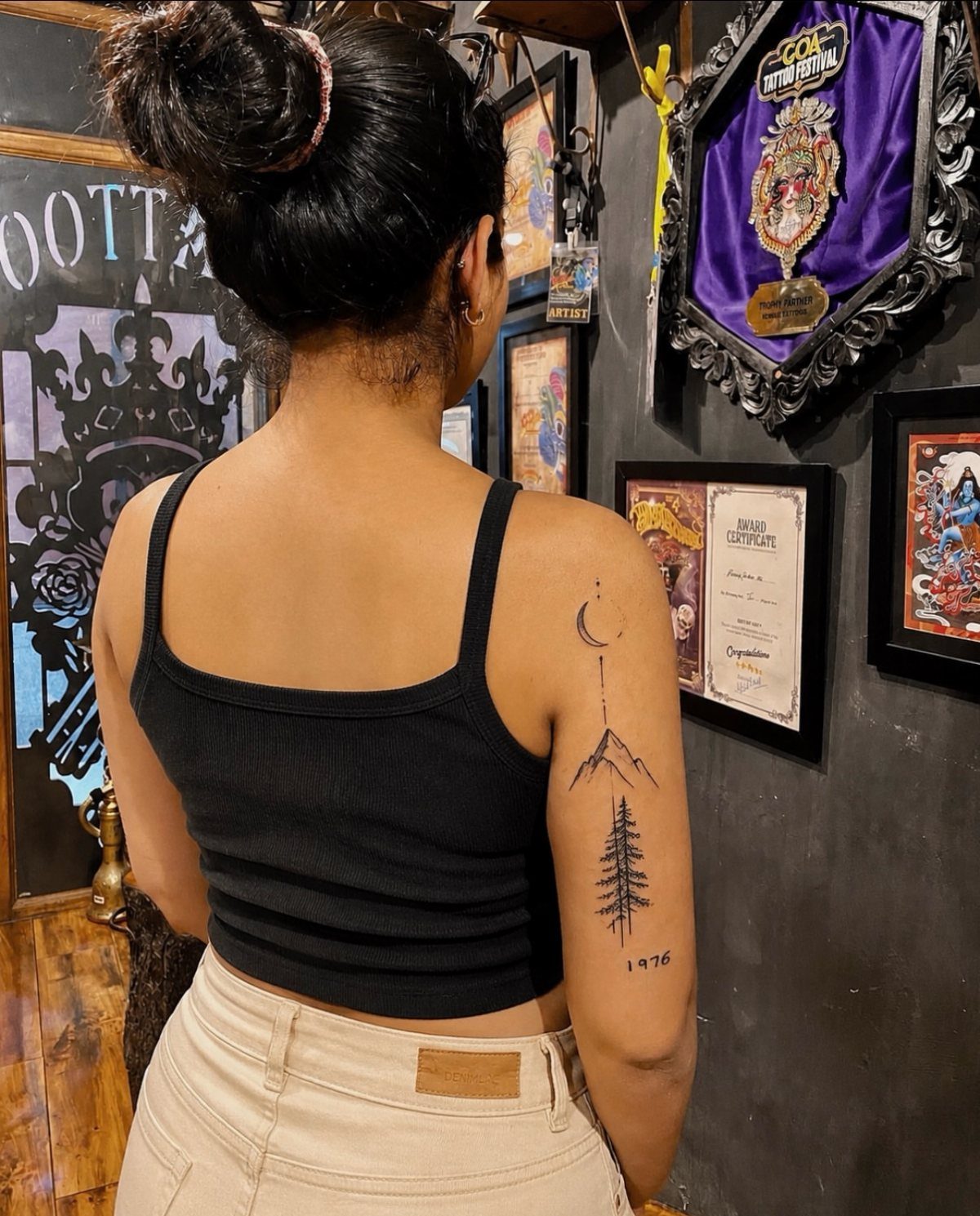 Woman showing a fine-line mountain and moon tattoo on her upper arm.
